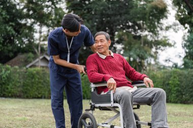 Sadık bir bakıcı, tekerlekli sandalyedeki yaşlı bir adamla özenli bir şekilde iletişim kuruyor, yemyeşil bir bahçede bakım ve bağlantı kuruyor..