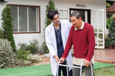 Şefkatli bir doktor, yaşlı bir adamın evinin önünde yürümesine yardım ediyor. Huzurlu bir bahçe ortamında bağımsızlığı teşvik ediyor..