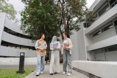 Kampüste birlikte yürüyen üç farklı kültürlü kadın akademik amaçlarını tartışırken dizüstü bilgisayar ve eğitim materyallerini mutlulukla taşıyorlar..