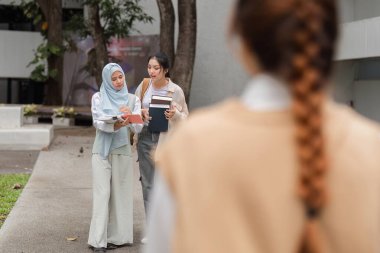 Farklı bir üniversite öğrencisi bir arkadaşıyla notlar alırken, başka bir öğrenci uzaktan izleyip işbirliği gösteriyor..