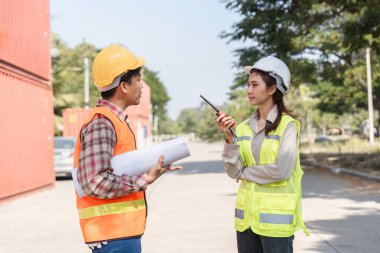 Bir lojistik mühendisi ve proje yöneticisi, inşaat sahasında iletişim için bir telsiz kullanarak proje sorunları hakkında ayrıntılı bir tartışmaya girişirler..