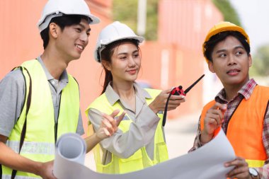 Üç inşaat işçisi, bir mühendis, bir proje yöneticisi ve bir işçi, yoğun bir şantiyede proje planları üzerinde işbirliği yapıyorlar..