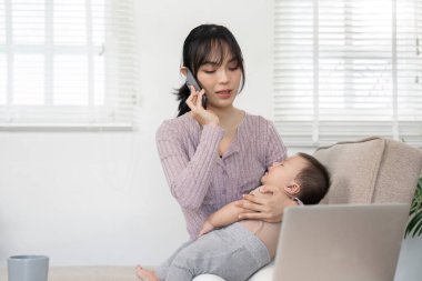 Odaklanmış bekar bir anne, bebeğini şefkatle tutarken bir iş çağrısına katılır, kariyer ve çocuk bakımını dengelemenin zorluklarını gösterir..