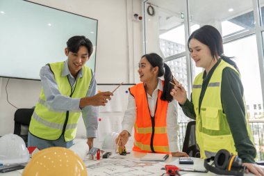 Canlı bir inşaat ekibi proje planlarını tartışırken hevesle beyin fırtınası yapıyor, ortak ofis ortamında takım çalışması ve yaratıcılık sergiliyor..