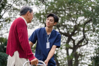 Huzurlu bir açık hava ortamında yaşlı bir adamla şefkatli bir sağlık çalışanı arasında neşeli bir etkileşim, destek ve bağlantı.