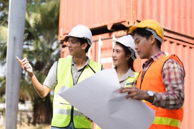 Aralarında bir mühendis, bir proje yöneticisi ve bir işçinin de bulunduğu üç kişilik bir inşaat ekibi, projenin detaylarını canlı bir şantiyede elinde planlarla tartışıyorlar..