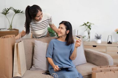 Neşeli kadınlar, birlikte online alışveriş deneyimlerinin keyfini çıkarırken, biri diğerine gülümserken, bir kredi kartı tutarken, kanepede neşeli bir anı paylaşırlar..