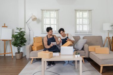 İki adam, rahat bir oturma odasında, çevrimiçi işleri için siparişleri paketlemek için birlikte çalışıyorlar, takım çalışması ve girişimcilik sergiliyorlar..