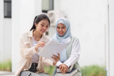 İki çok kültürlü kadın açık havada bir çalışma seansında notlarını paylaşıyor ve dost canlısı ve işbirlikçi bir atmosferde fikirleri tartışıyorlar..