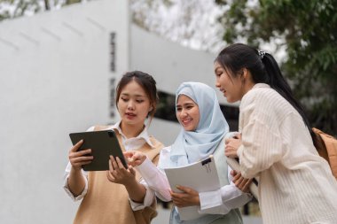 Açık havada tablet etrafında işbirliği yapan, fikirleri paylaşan ve canlı bir akademik ortamda birlikte eğitim gören üç farklı kız öğrenci..