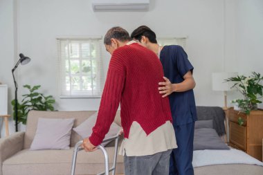 Şefkatli bir hemşire yaşlı bir adama rahat bir ev ortamında yürüteç kullanmasında yardımcı olur. Hareket halinde bakım ve destek gösterir..