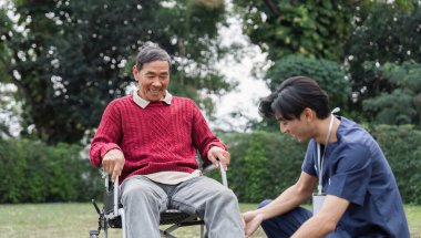 Kırmızı kazaklı yaşlı bir adam, huzurlu bir bahçede şefkatli bir sağlık görevlisiyle, dostluğu ve empatiyi simgeleyen neşeli bir anı paylaşıyor..