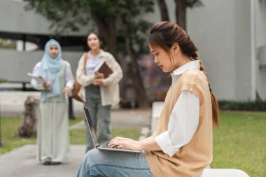 Arkadaşları canlı bir kampüs ortamında akademik adanmışlık gösterirken, çeşitli bir üniversite öğrencisi dışarıda dizüstü bilgisayar eğitimi alıyor..