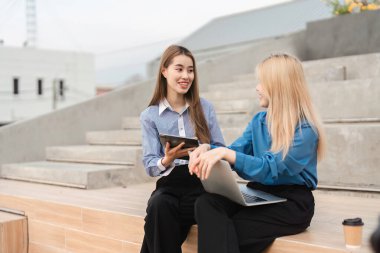 Açık havada otururken tablet ve laptop üzerinde işbirliği yapan iki farklı iş kadını, profesyonel bir ortamda yenilikçi fikirleri paylaşıyorlar..