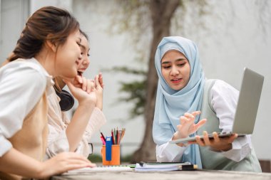 Aralarında tesettürlü Müslüman bir kadının da bulunduğu çeşitli kız öğrenciler açık havada dizüstü bilgisayar kullanırken fikirlerini tartışarak grup çalışması yapıyorlar..