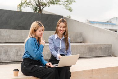 İki farklı iş kadını, profesyonel bir ortamda fikirlerini paylaşırken dışarıda dizüstü bilgisayar kullanıyorlar..
