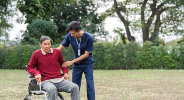Sakin bir açık hava ortamında, hemşire yardımcısı tekerlekli sandalyedeki yaşlı bir adamı destekliyor ve bakım ve arkadaşlığın önemini vurguluyor..