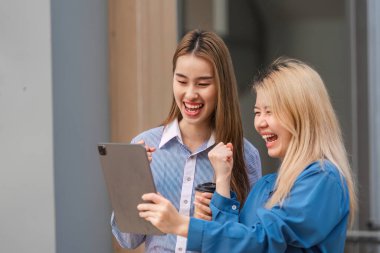 İki farklı kadın bir tablete bakıp kahve içerken, takım çalışmasını ve pozitifliği ön plana çıkarırken birlikte bir başarıyı neşeyle kutluyorlar..