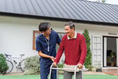 Şefkatli bir sağlık hizmeti sağlayıcısı yaşlı bir adama büyüleyici bir evin önünde yürüteci ile yardım ederken cesaret verici bir şekilde gülümsüyor ve destekleyici bir ilişki kuruyor..