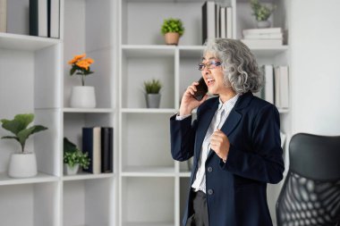 Tutkulu bir telefon görüşmesine katılmış yetenekli bir üst düzey işletmeci raflar ve yeşilliklerle çevrili şık bir ofiste duruyor..