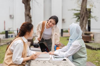 Aralarında tesettürdeki bir kadının da bulunduğu üç farklı kadın, açık havada bir çalışma grubuna katılıyor, fikirleri paylaşıyor ve akademik uğraşlarında karşılıklı destek sağlıyorlar..