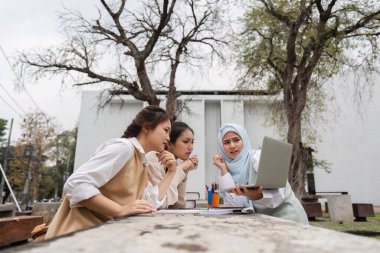 Üç çok kültürlü kadın dışarıda iş birliği yapıyor, verileri analiz ediyor ve yaratıcı bir ortamda bir çalışma sırasında bir dizüstü bilgisayardan bilgi paylaşıyorlar..