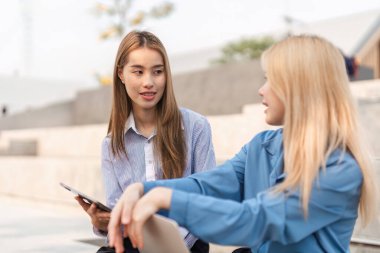 İki farklı kadın arkadaşça sohbet ederken, biri tablet tutuyor ve açık havada işbirliğini teşvik ediyor..