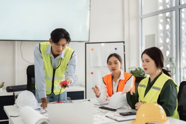 Çeşitli inşaat profesyonellerinden oluşan bir grup, parlak ve modern ofis ortamında güvenlik teçhizatı kullanarak ölçüm ve tasarımlar inşa etmede işbirliği yapıyor..