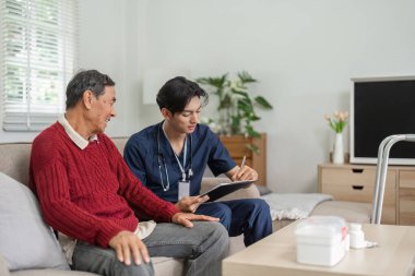 Bir hemşire, rahat bir ev ortamında yaşlı bir hastayla dostça bir konuşma yaparken bakım belgesi yazar..