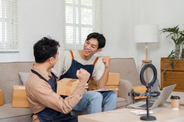 İki hevesli sosyal medya pazarlamacısı, rahat ofislerinde canlı yayınlanan bir canlı yayın sırasında başarılı ürün gösterileri üzerine neşeli jestlerle kutlama yapıyorlar..