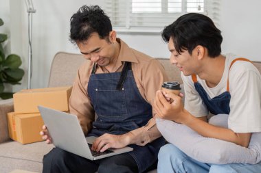 İki neşeli teslimatçı, biri elinde kahve fincanı olan, içi paket dolu rahat bir ofiste dizüstü bilgisayarda siparişleri inceleyen..
