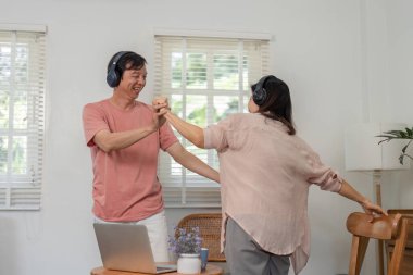 Neşeli yaşlı bir çift, kulaklık takarken, müzik dinlerken ve rahat evlerinde birbirlerine eşlik ederken eğlenceli bir şekilde dans eder..