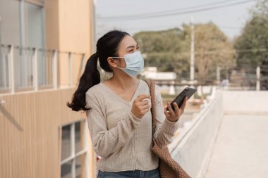 Maske takan ve elinde akıllı bir telefon tutan farklı bir kadın şehir merkezinde açık havada sohbet ediyor..