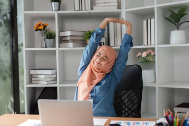 İş molası sırasında masasında uzanan ve gevşeyen, tesettürlü Müslüman bir kadın..