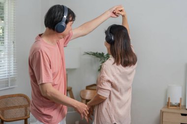 Olgun bir çift, evde kulaklık takmış, neşeli bir şekilde dans ediyor. Birbirleriyle olan bağlarını neşeli bir anda kutluyorlar..