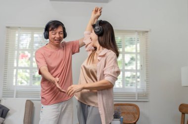 Mutlu yaşlı bir çift oturma odasında birlikte dans eder, kulaklık takar ve keyifli bir anı paylaşırken müziğin tadını çıkarır..