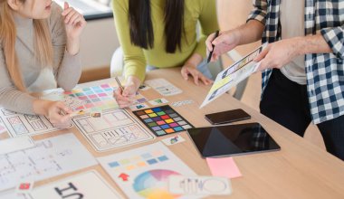 Tasarım materyalleri üzerinde işbirliği yapan, renkleri analiz eden ve modern bir ofisteki bir masada konseptleri tartışan farklı bir ekibin yakın plan görüntüsü..