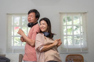 Neşeli bir çift arka arkaya dans ediyor, rahat evlerinde kulaklıklarla müzik dinliyor..