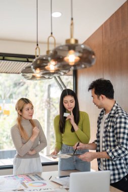 Çeşitli bir ekip tasarım fikirlerini tartışıyor ve modern ofis alanındaki materyalleri gözden geçiriyorlar..