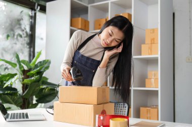 Bir e-ticaret işkadını paketleri tarıyor ve modern ofis ortamında birden fazla iş yaparken çevrimiçi siparişleri idare ediyor..