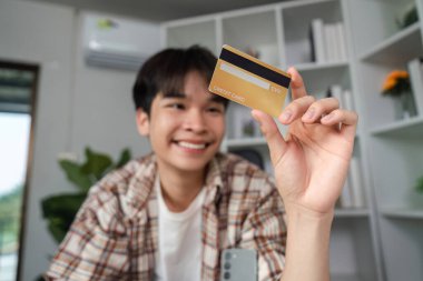 Neşeli genç bir adam kredi kartını gösteriyor, finansal gücü ve online alışverişin kolaylığını temsil ediyor..
