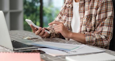 Odaklanmış bir kişi, finansal belgeleri incelerken akıllı telefon ile iletişim kurar, teknolojinin çalışmalarına entegrasyonunu vurgular.