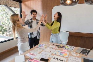 Takım çalışmasını ve yaratıcı işbirliğini gösteren canlı bir ofiste üç hevesli iş arkadaşı beşlik çaktı..