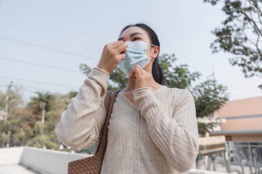 Genç bir kadın kamuya açık alanda günlük rutininde sağlık ve güvenlik uygulamalarını vurgulayarak koruyucu maskesini takıyor..