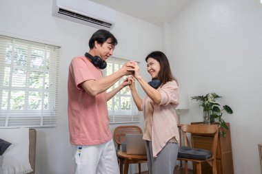Orta yaşlı mutlu bir çift oturma odalarında el ele dans ederken, kulaklık takarken ve sıcak bir atmosferde paylaşılan keyifli bir anın tadını çıkarırken..