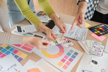 Bir ofis çalışma alanındaki beyin fırtınası sırasında tasarım modellemelerini ve renk paletlerini inceleyen çeşitli bir ekip üyeleri grubu.