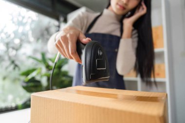 A close-up of an e-commerce businesswoman scanning a package with a barcode scanner while managing her online store in a modern workspace. clipart