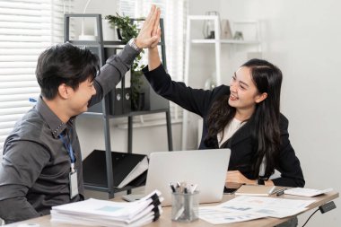 İki iş adamı, modern ofis ortamında takım çalışmalarını ve başarılarını kutlamak için beşlik çakıyor..