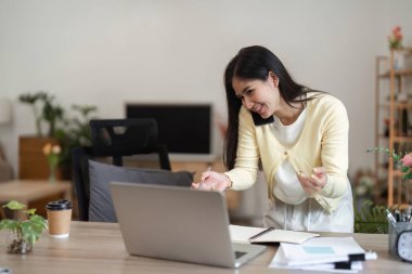 Genç bir profesyonel, dizüstü bilgisayarıyla iletişim kurarken telefonda heyecanlı bir şekilde konuşur, evden eve dinamik bir çalışma tarzını vurgular..
