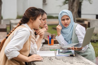 Aralarında tesettürlü bir kadının da bulunduğu çeşitli bir grup kız öğrenci, bir çalışma sırasında yoğun bir şekilde bilgisayar ekranına odaklanmış, işbirliği ve nişanı resmediyor..